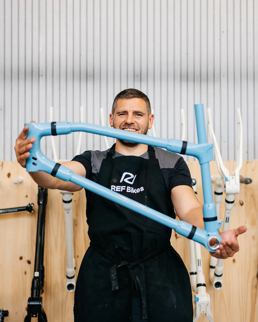 Un artisan en tablier REF Bikes tient un cadre de vélo