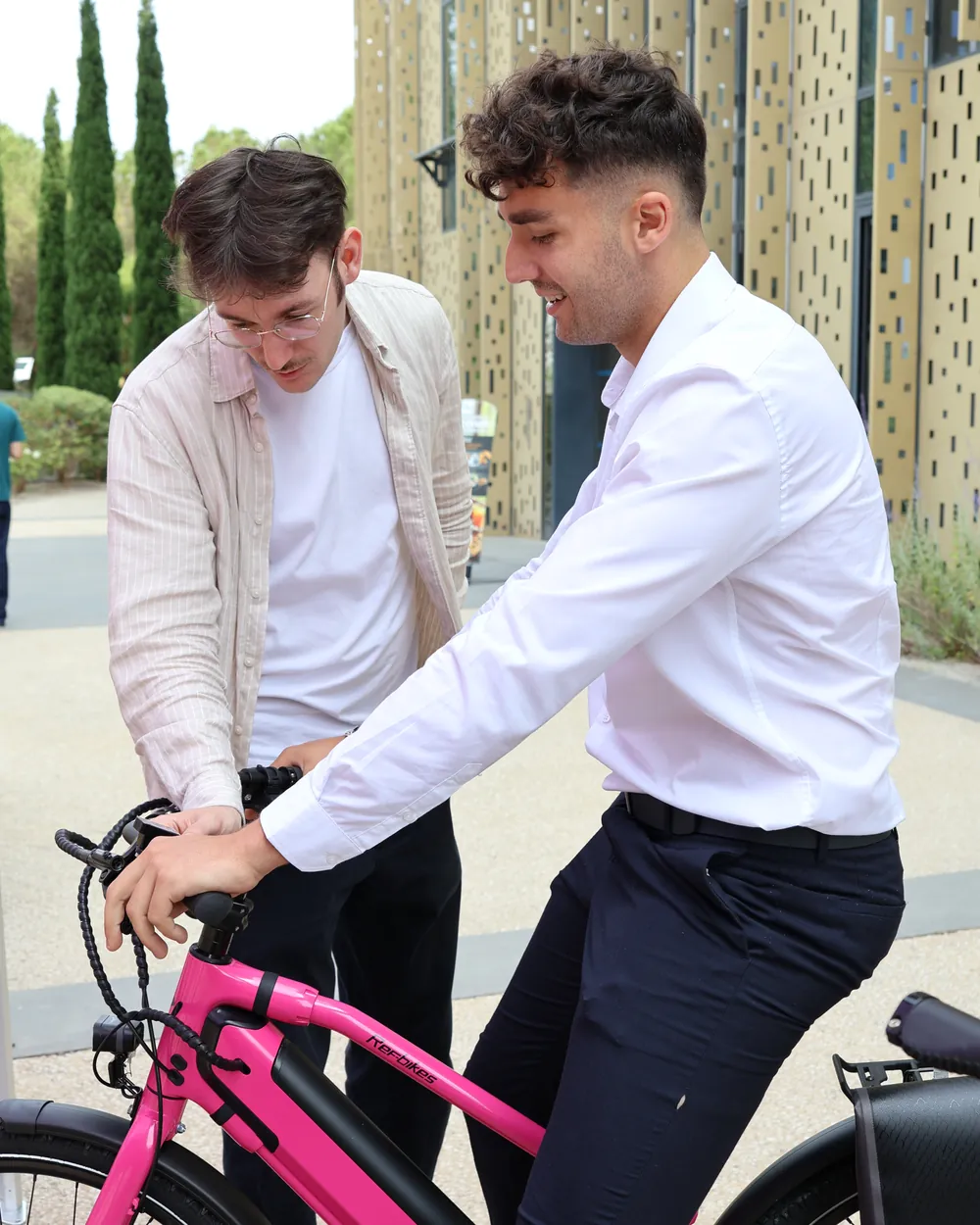 Devant leurs bureaux, un salarié en chemise essaie un vélo REF Bikes pendant qu'un collègue le lui présente